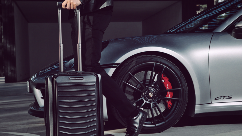 Shows Picture of man-infront-silver-porsche-with-hardcase-suitecase.png