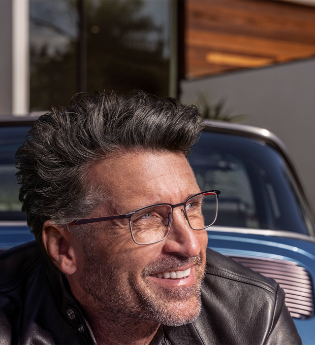 Shows Picture of Patrick-Dempsey-wearing-glasses-infront-blue-porsche-smiling.png